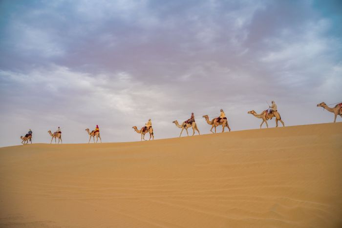 Handler leading a camel with a visitor at a desert safari camp near Dubai, showing the safe mounting position