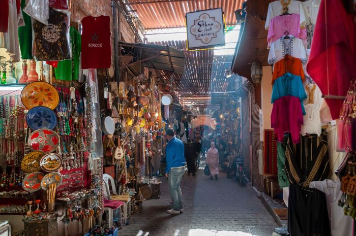 Narrow covered souk alley in the Marrakech medina with lanterns and shafts of light through the roof slats